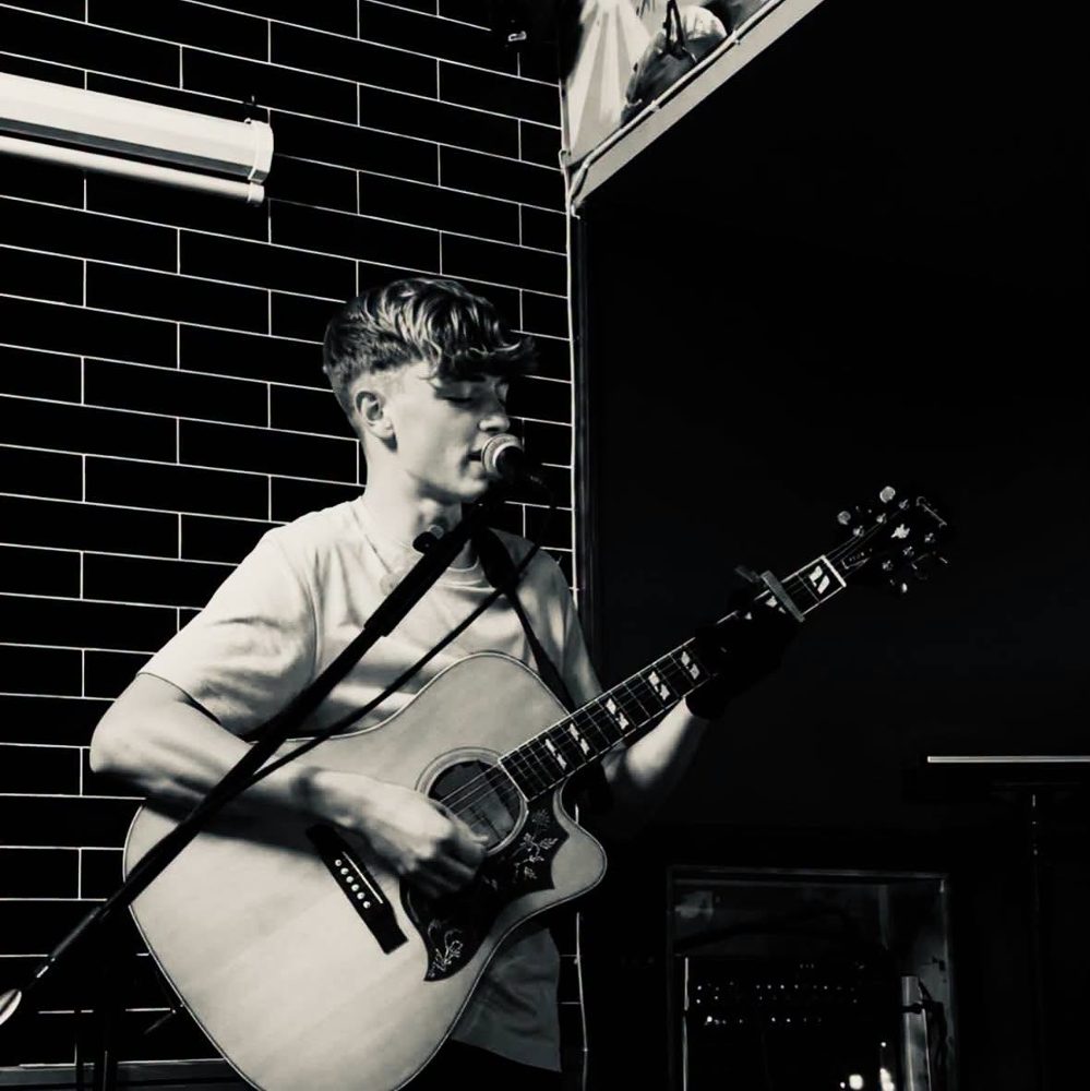 Black and white photo of Harvey Ralphs playing acoustic guitar on stage