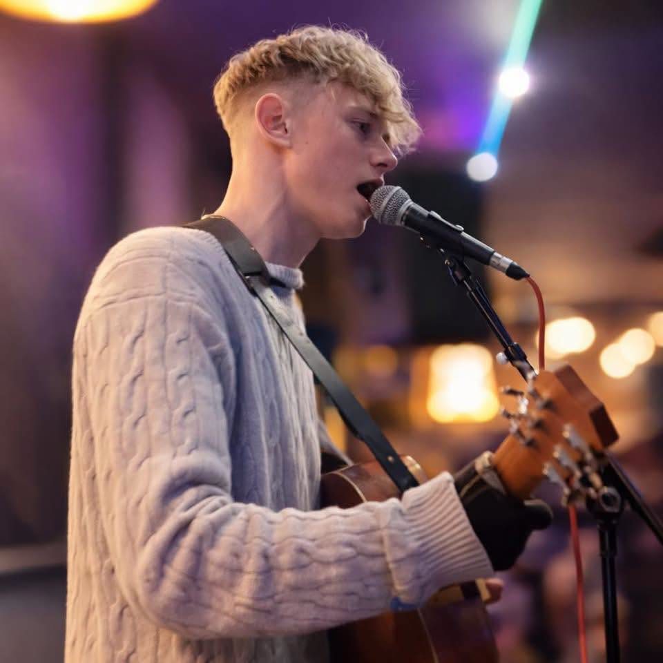 Harvey Ralphs singing into a microphone with an acoustic guitar